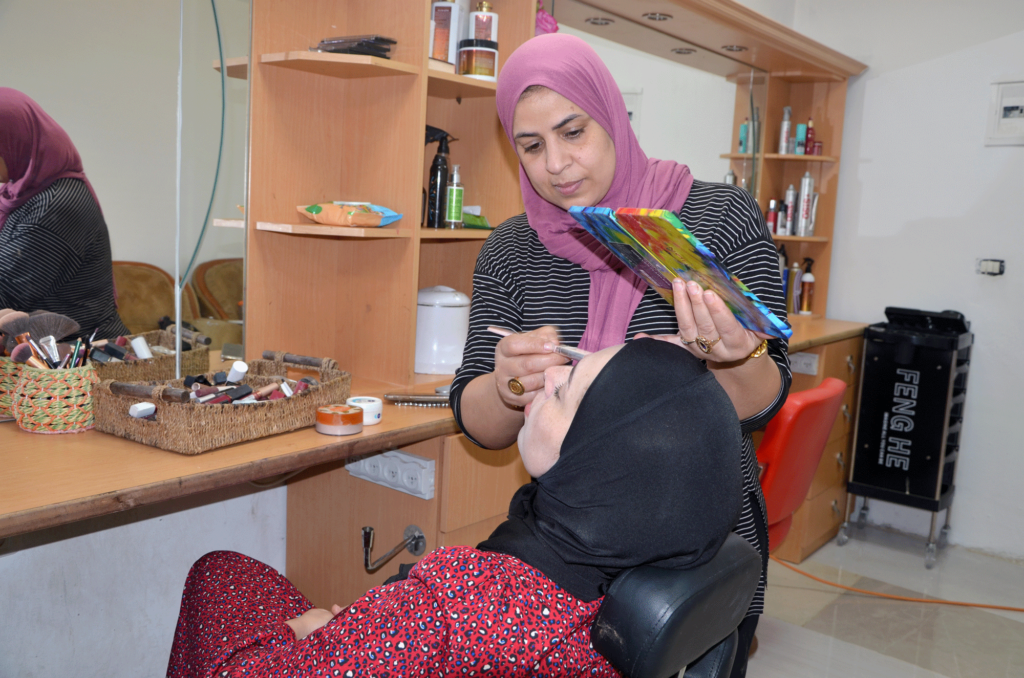 Fayrouz applies makeup to a client in a chair.