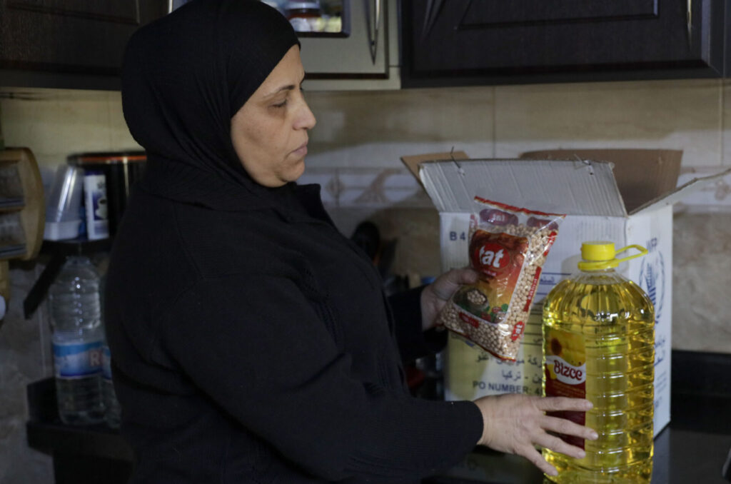 A mother in her kitchen unpacks the food from the parcel she just received from Anera.