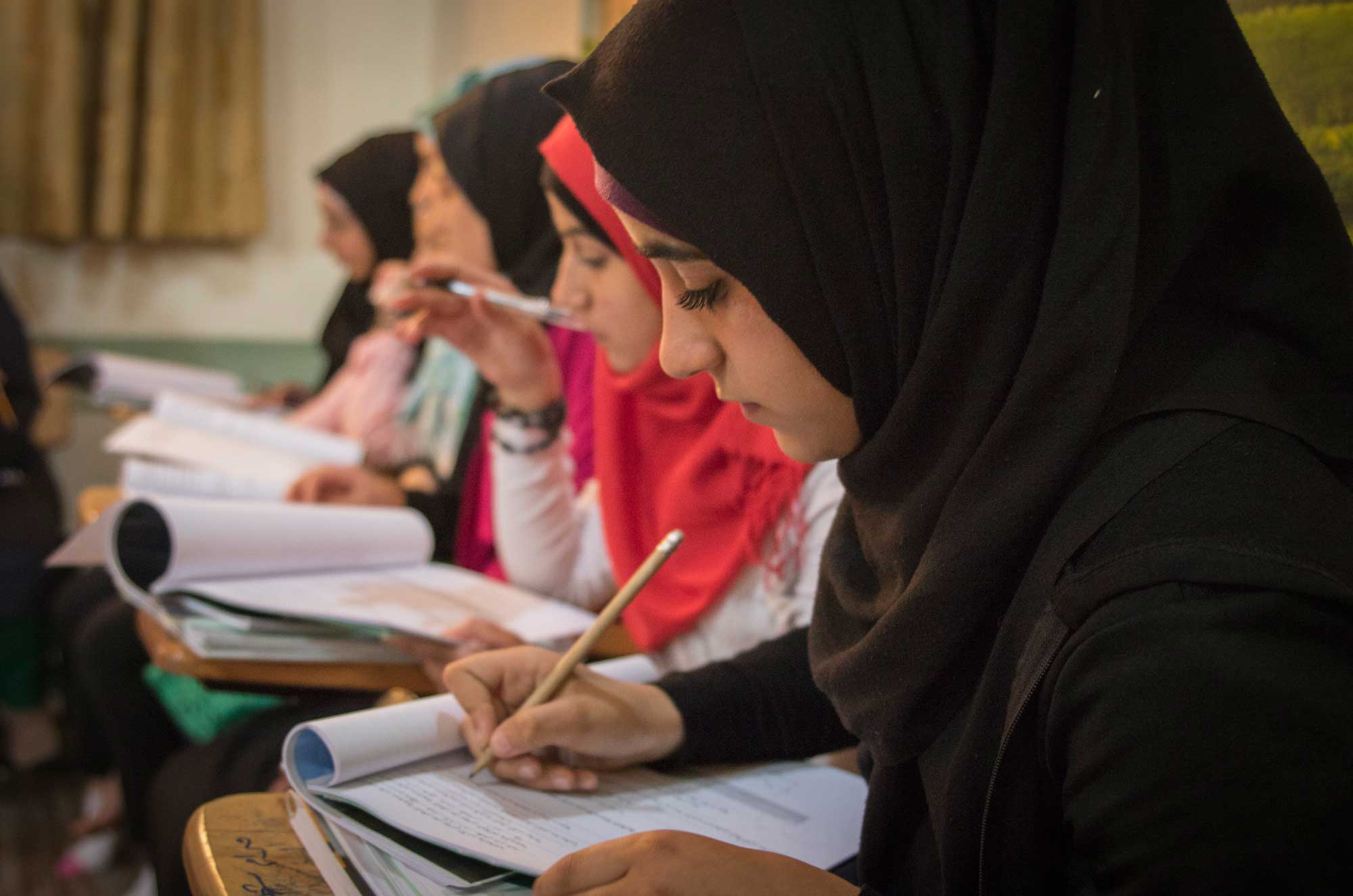 Anera-basic-math-class-Baalbeck A group of Syrian refugee girls are in writing in their notebooks during one of Anera's basic ed classes in Baalbek.