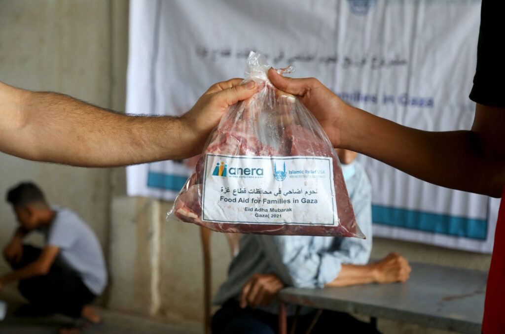 A volunteer passes a bag of meat that says Anera, Food Aid for Families in Gaza, to a young child.