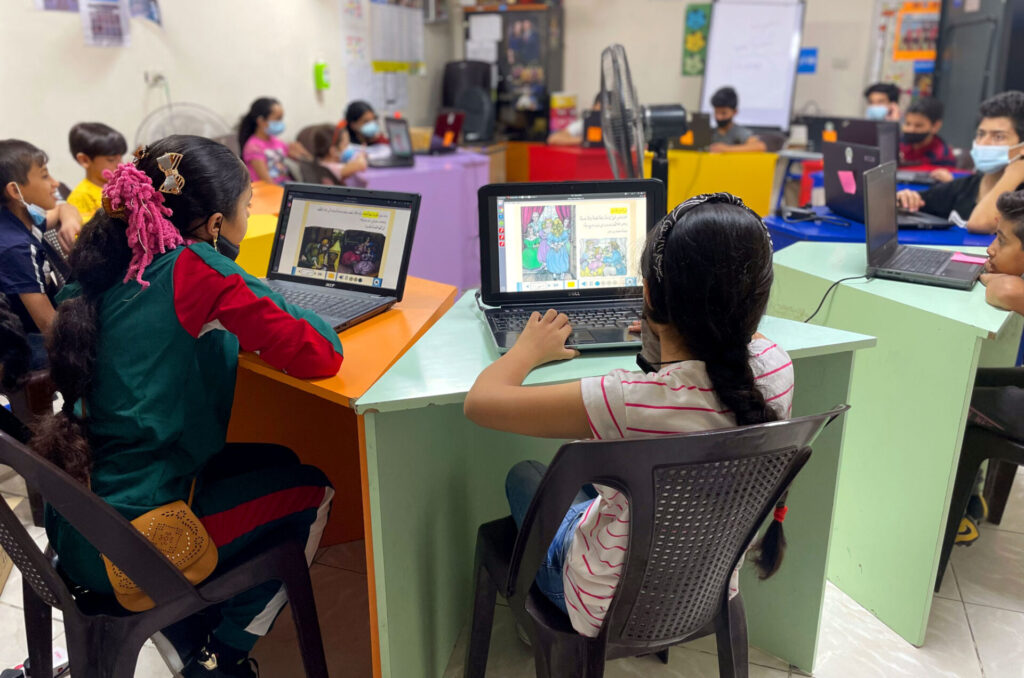 Students sit at desks in a circle with laptops.