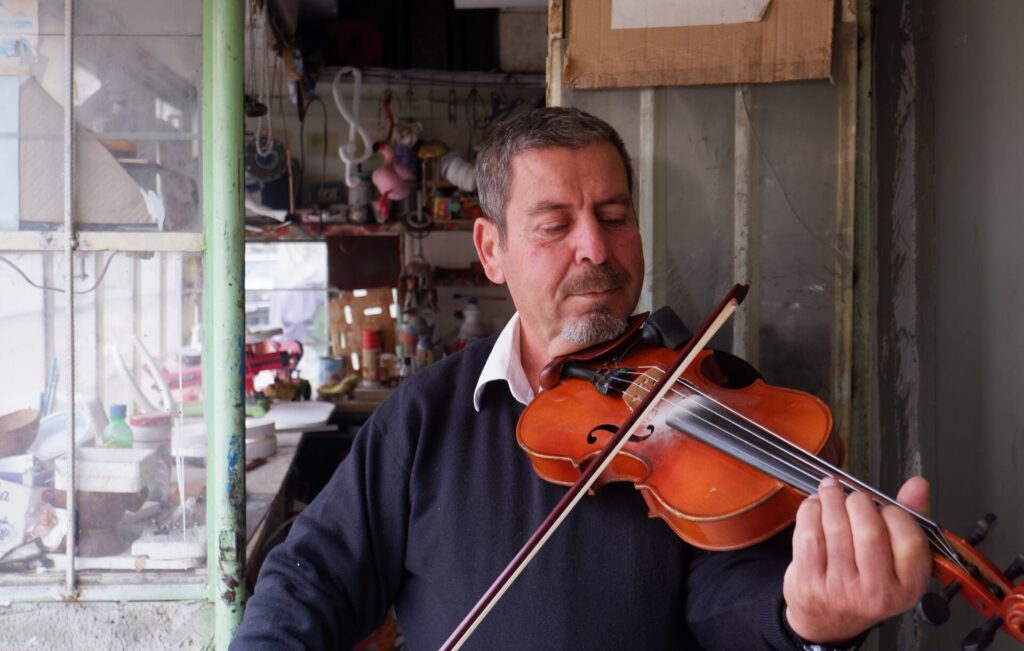 A man plays the violin in front of his house.