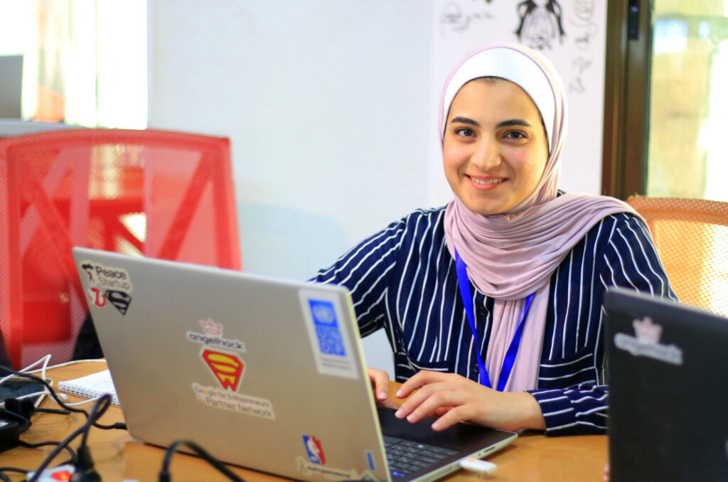 A woman sits alone and smiles for the camera with her computer.