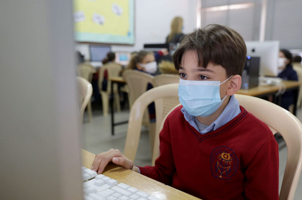A boy wearing a mask works alone on his computer in his classroom.