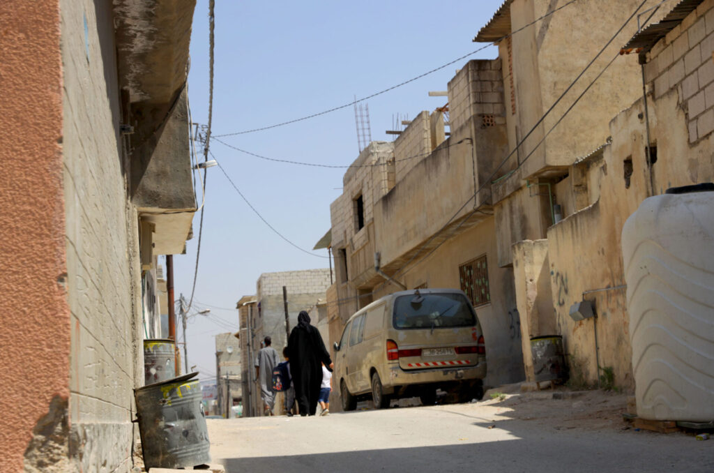 A street in Jerash Camp, Jordan, with a car and a lone walker.
