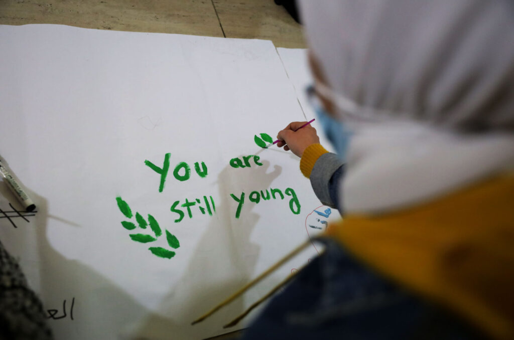 From over a girl's shoulder, we see her painting the words "You are still young."