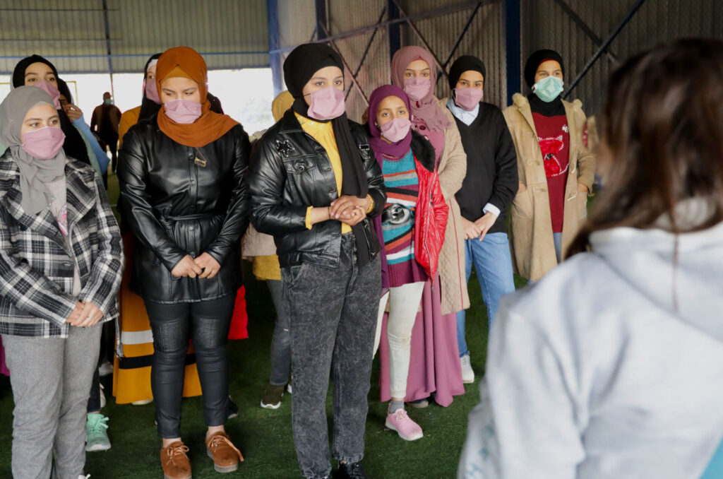 A group of girls stand and receive instruction as part of their education.