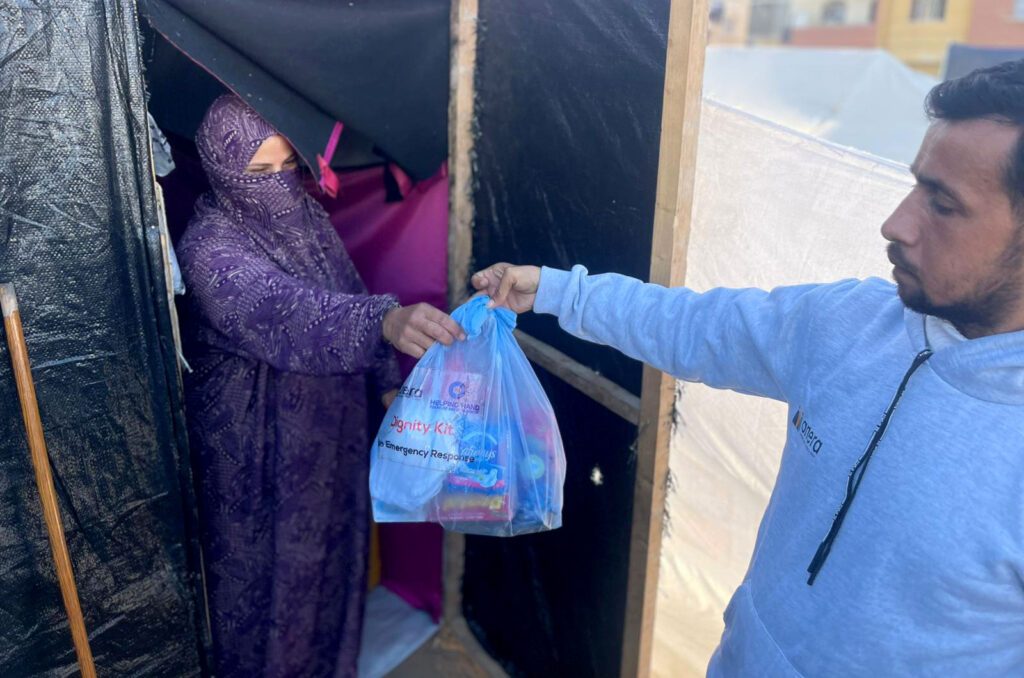 An Anera volunteer hands a dignity kit to a woman in a tent