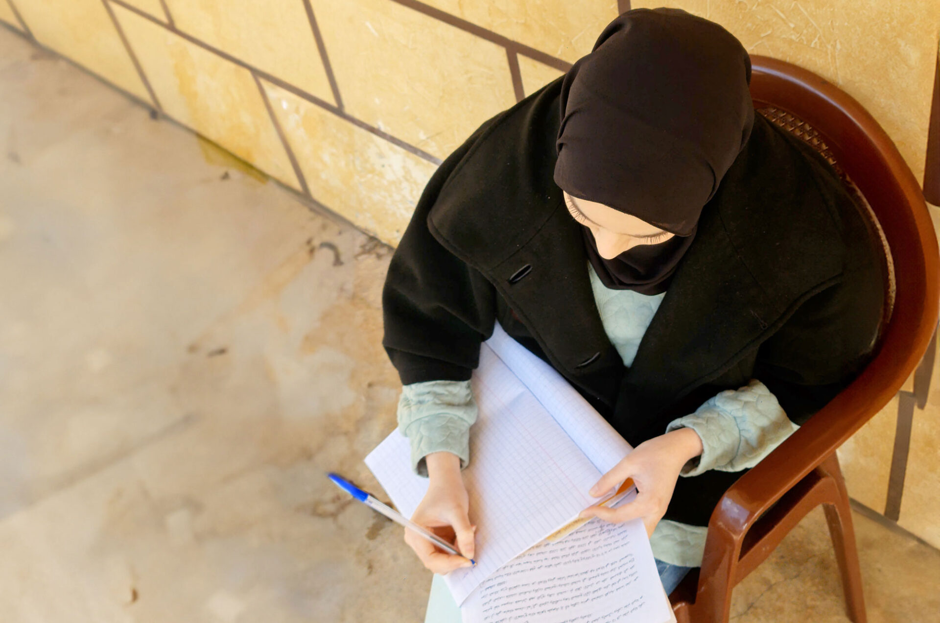 A girl wearing a hijab bends over a notebook.
