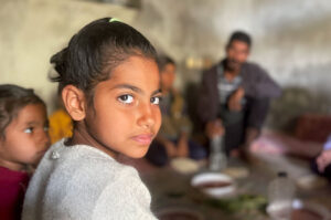 A young girl sitting in the circle of family members stares directly into the camera.