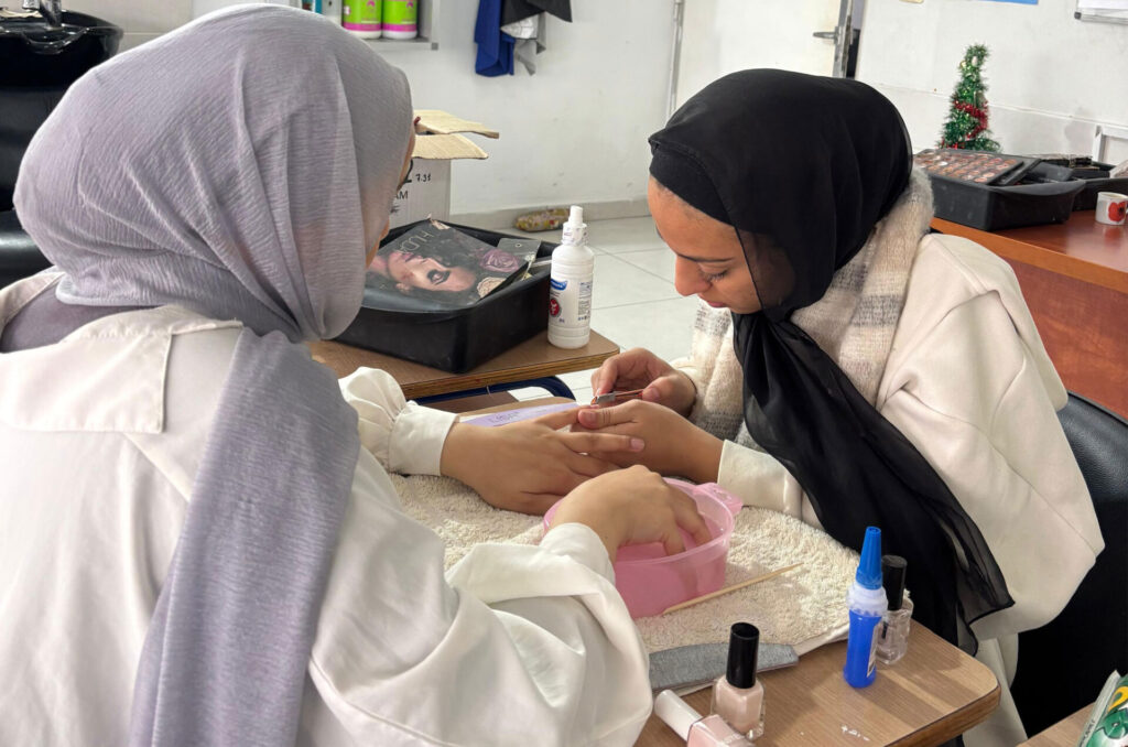 A student in Anera's beauty course manicures another student.