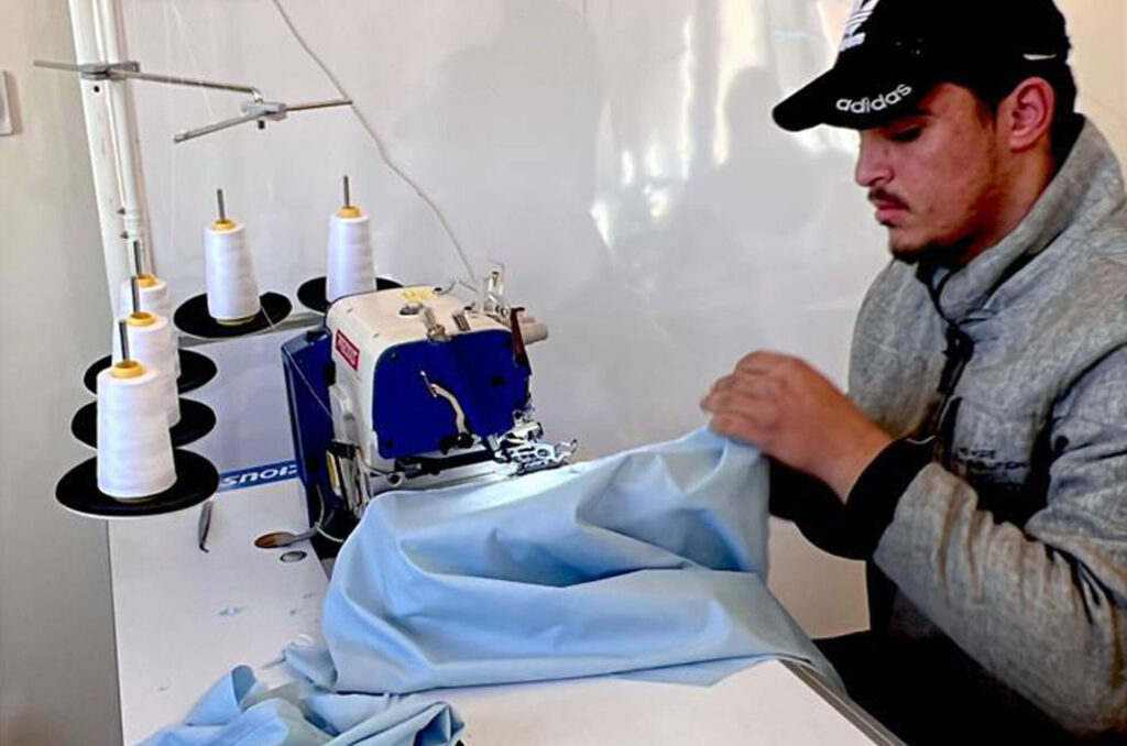 A student in Anera's sewing course uses a sewing machine to stitch a school uniform.