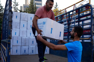 A humanitarian aid worker hands a box of UNICEF aid to another aid worker