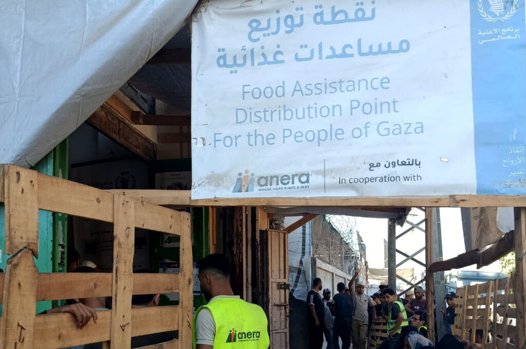 Workers and recipients gather at a distribution site with a banner reading "Food Assistance Distribution Point for the People of Gaza."