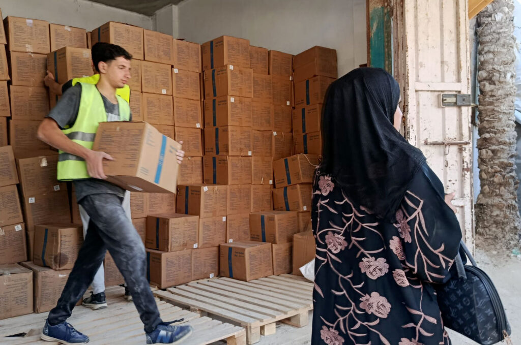 A worker carries a food parcel from the stacks of parcel boxes behind him.