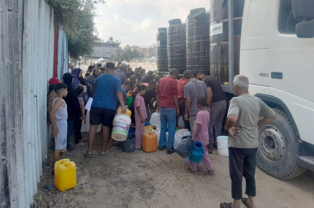 A crowd queues with buckets at a water truck to collect water for their families today.