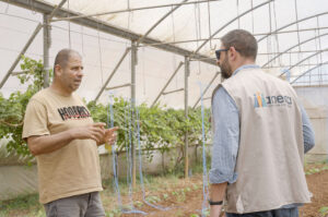 An Anera staffer speak with a man participating in the Ventures program in his greenhouse.