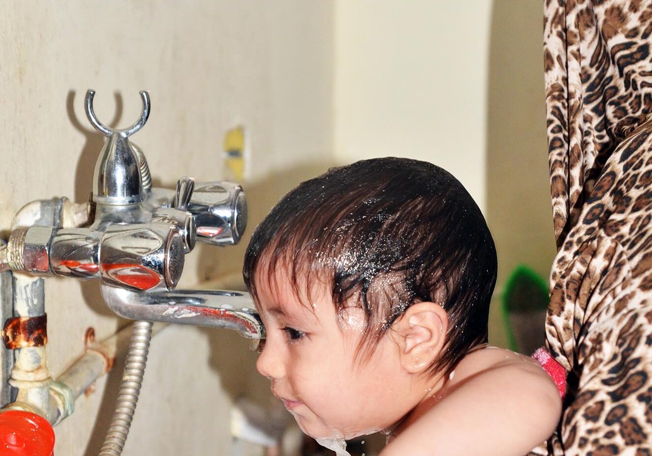 Ibtisam's son bathing under the faucet which was recently connected clean water